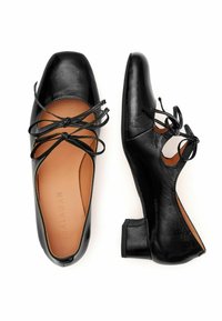 Ballerine in pelle nera con punta quadrata, design con lacci, lati ritagliati e tacco basso a blocco. L'interno presenta una fodera in pelle color tan.