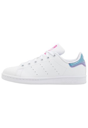 Zapatilla blanca de caña baja con franjas laterales perforadas, cordones blancos, etiqueta rosa en la lengüeta y detalle iridiscente azul-púrpura en el talón.