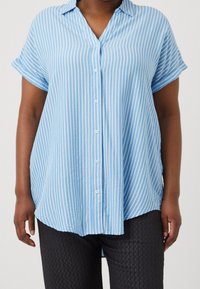 Ljust blå kortärmad skjorta med vita vertikala ränder, med krage och knappframsida. Tyget verkar mjukt och lättviktigt.