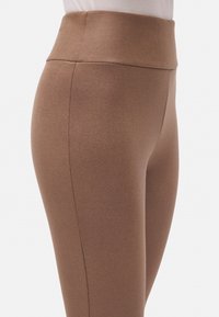 Leggings marrones de cintura alta con una textura suave y un diseño ajustado, que presentan una costura que recorre el lateral para un toque adicional.