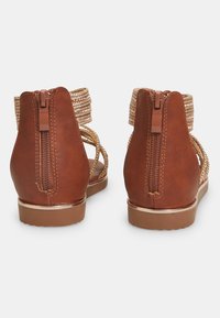 Ruske syntetiske lærsandaler med lav hæl, gyldne flettede remme og en bageste lynlås, der har en glat tekstur og et enkelt design.