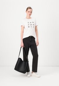 T-shirt bianco con simboli grafici neri, pantaloni in denim neri e una grande borsa in pelle nera. Le sneakers bianche completano l'outfit.
