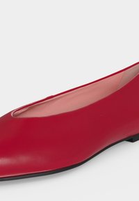 Chaussure plate de ballet en cuir rouge avec un bout rond, une doublure rose clair et une semelle noire basse.