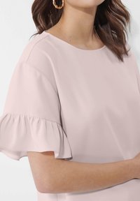Helle rosa Bluse mit kurzen, rüschierten Ärmeln und rundem Ausschnitt. Glatte Textur, lässiges Design und eine schlichte Silhouette.