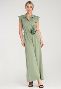 Zielony kombinezon z kołnierzykiem, krótkimi rękawkami, guzikiem z przodu, paskiem w talii i falbaniastym detalem w kształcie kwiatu; miękka tkanina i szerokie nogawki.