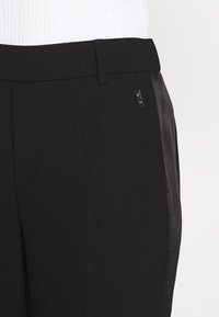 Zwarte broek met een gladde textuur, slim fit en een glanzend zijpaneel. Heeft een riemlus en een zilveren logo-accent op de tailleband.