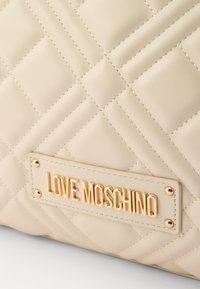 Borsa in ecopelle beige trapuntata con placca logo in tonalità oro e cuciture decorative. Texture liscia con audace motivo a diamante.