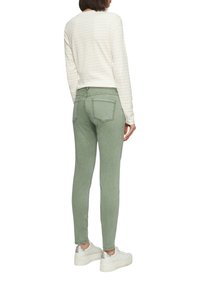 Jasnozielone jeansy slim fit z tylnymi kieszeniami i detalami w szwie, zestawione z kremową, paskowaną koszulą z długim rękawem oraz białymi trampkami na platformie.