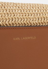 Lähikuva tan-värisestä kudotusta kankaasta ruskean nahkan päällä, jossa on kultakirjaimin painettu "KARL LAGERFELD" nahkapinnalle.