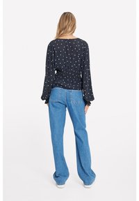 Sort bluse med polkaprikker og samlet talje, lange ærmer. Kombineret med lyseblå vide jeans og hvide sneakers.