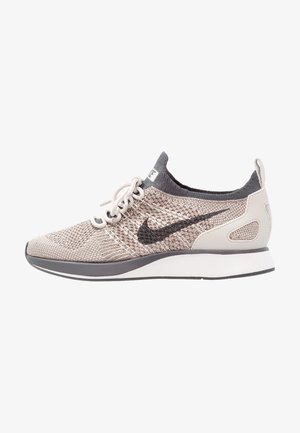 Chaussure de course Nike tricotée beige clair et grise avec logo swoosh noir, lacets blancs et semelle blanche rembourrée.