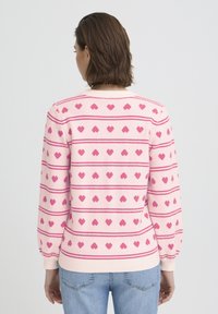 Pull rose présentant un motif rayé avec de petits cœurs, poignets et encolure côtelés, complétant une texture en maille douce.