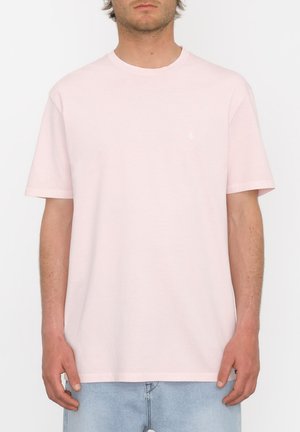 T-shirt rose clair à manches courtes en coton doux. Présente un col rond et un petit logo de marque sur la poitrine. Design simple.
