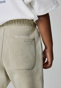 Svetlozelené bavlnené jogger nohavice s textúrovaným povrchom, so vyšívaným logom "ALLSAINTS" na zadnej vrecku a elastickým pásom.