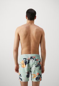 Shorts de înot pentru bărbați dintr-un material verde mint deschis, cu un model tropical de flori în nuanțe de portocaliu și verde închis. Talie elastică cu detalii la buzunarul din spate.