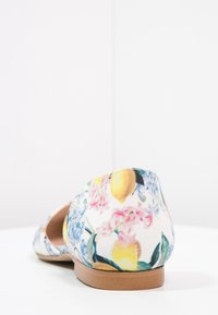 Chaussure plate fleurie en tissu blanc avec des citrons jaunes et des fleurs roses, dotée d'un bout arrondi et d'une semelle en caoutchouc marron.