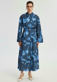 Denim shirt dress with a blue cloud pattern, long sleeves, button-down front, waist belt, and a relaxed fit, reaching mid-calf length.