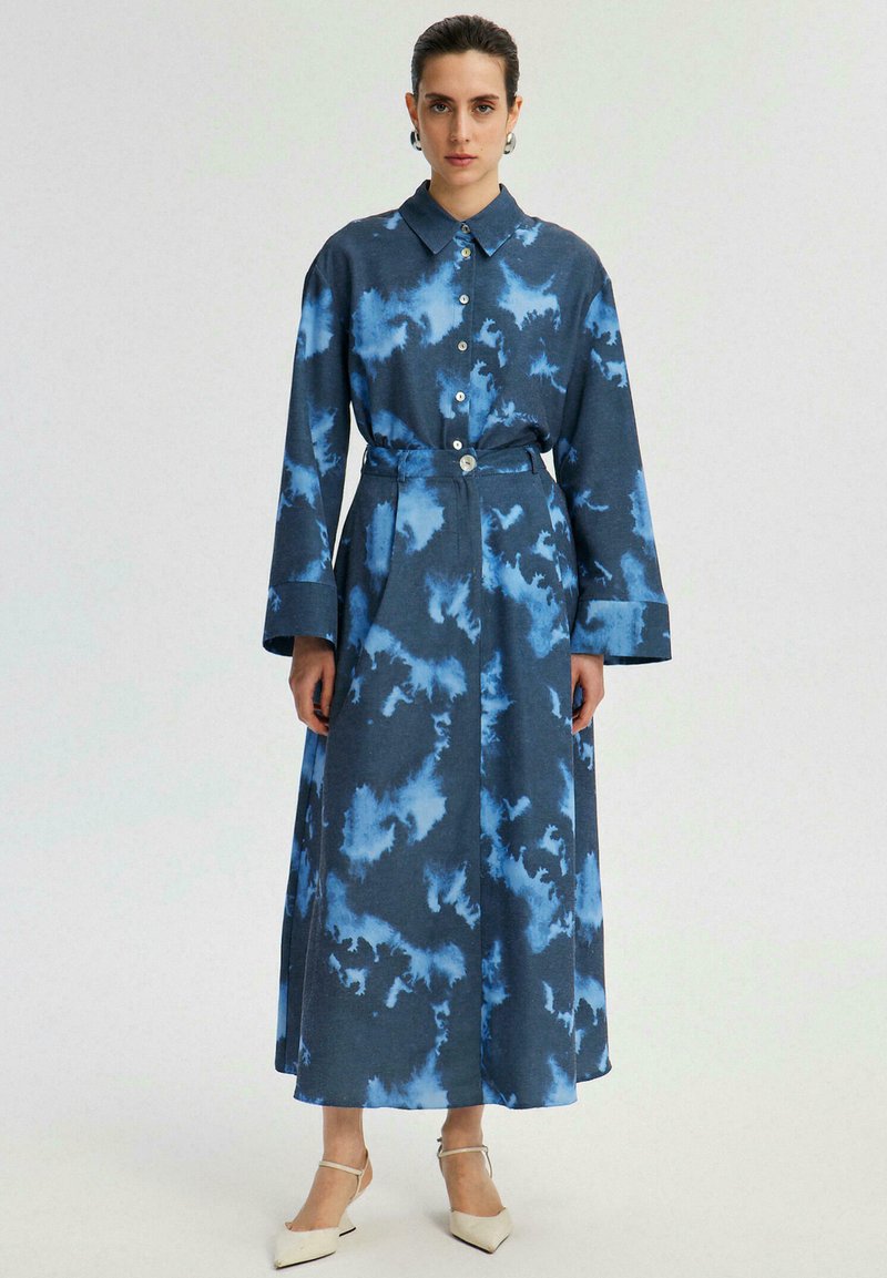 Robe en jean avec un motif de nuages bleus, manches longues, boutonnage à l'avant, ceinture à la taille, et une coupe décontractée, atteignant la longueur mi-mollet.