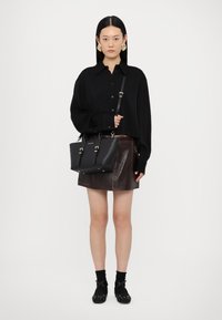 Schwarze Lederhandtasche mit goldenen Beschlägen, verstellbarem Tragegurt und strukturiertem Design, kombiniert mit einem schwarzen Oversized-Hemd und einem braunen Lederrock.