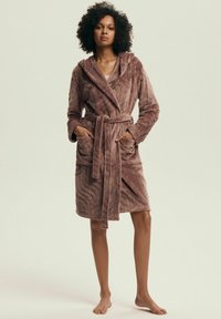 Pluszowy fioletowy szlafrok o teksturowanym, falistym wzorze, z długimi rękawami, kapturem i wiązanym paskiem. Posiada dwie przednie kieszenie.