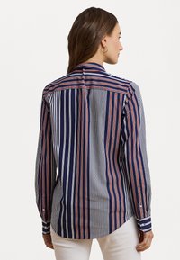 Camicia a maniche lunghe a righe blu navy, bianche e rosse. Presenta un colletto e polsini zapponati, con orlo curvo e texture del tessuto morbida.