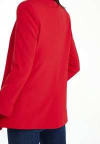 Rød skræddersyet blazer med et rent design, strukturerede skuldre og lange ærmer. Har et glat stof og sidelommer.