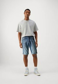 Szary t-shirt z krótkim rękawem, niebieskie szorty jeansowe z podwiniętymi brzegami oraz jasnoniebieskie trampki za kostkę. Prosty fason, casualowy krój.