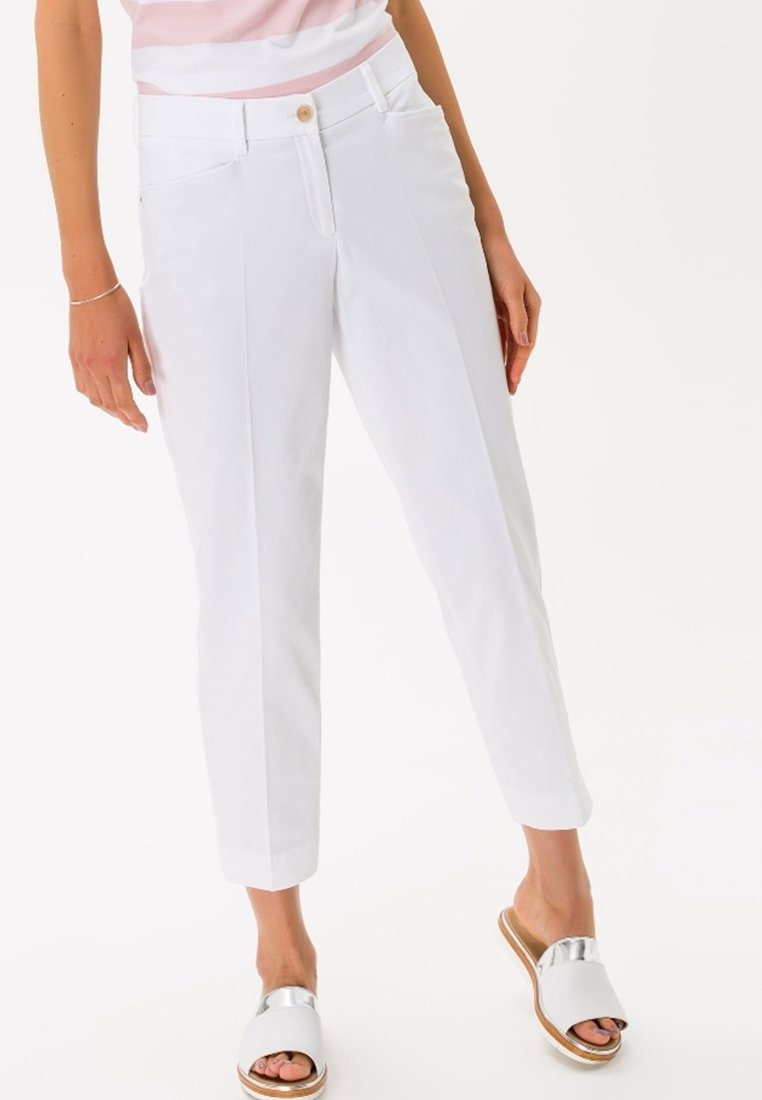 Femme portant un pantalon blanc sur mesure longueur cheville avec un bouton et des poches, associé à des sandales argentées et blanches à bout ouvert.