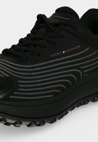 Μαύρο αθλητικό παπούτσι Tommy Hilfiger με μαύρα κορδόνια, γκρι κυματιστά σχέδια στο πλάι και υφασμένο πέλμα.