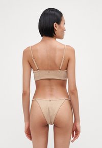 Rødt bikinitsett i beige og krem, med tynne stropper og et minimalistisk design. Materialet ser mykt ut med en glatt tekstur.