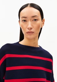 Marineblauwe gebreide trui met horizontale rode strepen, wijde halslijn en zachte textuur. Close-up van het kledingstuk zonder afleidingen.