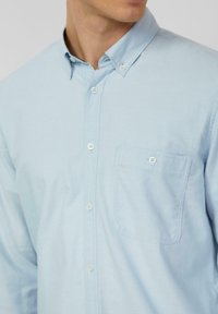 Chemise bleu clair à boutons avec col classique, poche poitrine et boutons blancs. Fabriquée en tissu tissé texturé.