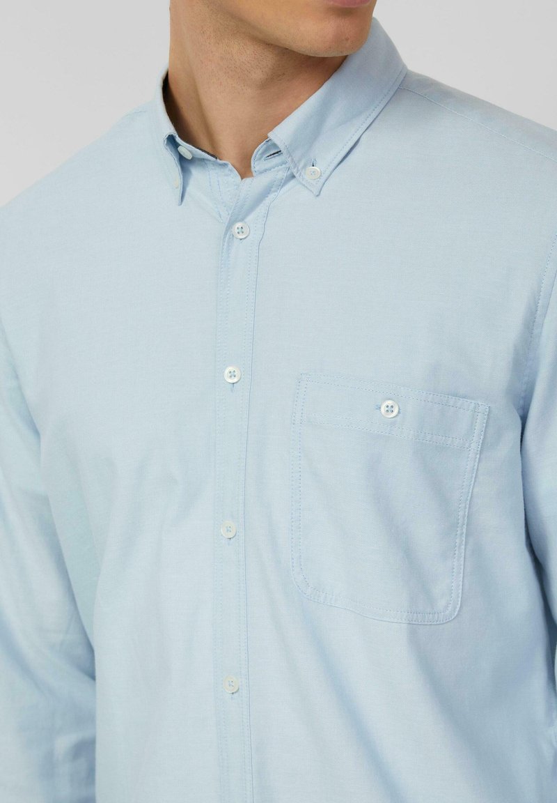 Chemise bleu clair à boutons avec col classique, poche poitrine et boutons blancs. Fabriquée en tissu tissé texturé.