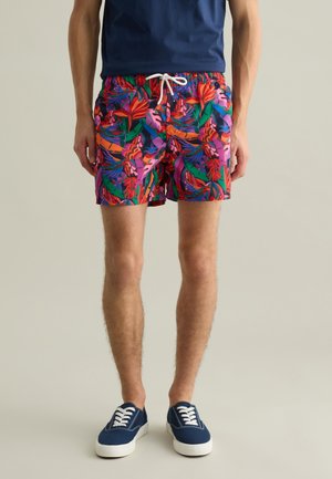 Herren-Badehosen mit mehrfarbigem Blumenmuster, ausgestattet mit einem Kordelzugbund, leichten Materialien und klassischer Passform, kombiniert mit navyblauen Schuhen.