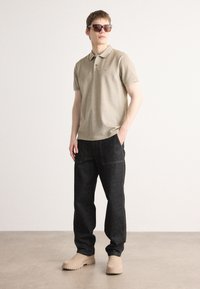 Beige polo shirt, mørke denim bukser og beige slip-ons. Skjorten har krave og subtile detaljer; bukserne har frontlommer.