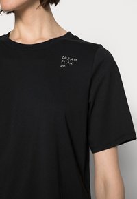 Camiseta de algodón negra con manga corta, con el texto impreso en blanco "SUEÑA. PLANEA. HAZ." situado en el hombro izquierdo.