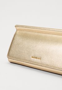 Pochette métallisée dorée avec une finition texturée. Présente une forme rectangulaire élégante et un détail de marque subtil à l'avant.
