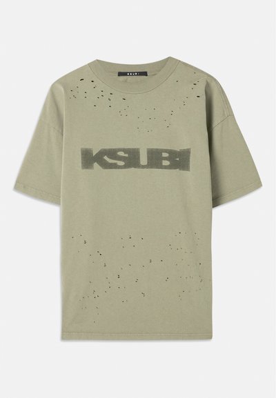 Olive zaļš īsu piedurknju T-krekls ar melnu "KSUBI" grafiku, nodilušu tekstūru ar maziem melniem punktiem un apaļu kakla izgriezumu.
