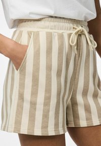 Shorts rayés beige et crème avec une texture douce, taille élastique et détail de cordon. Comprend des poches latérales et une coupe décontractée.