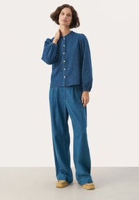 Džínový outfit so priliehavou košeľou na gombíky s naberanými rukávmi a voľnými širokými nohavicami v zodpovedajúcej modrej farbe. Mäkká textúra.