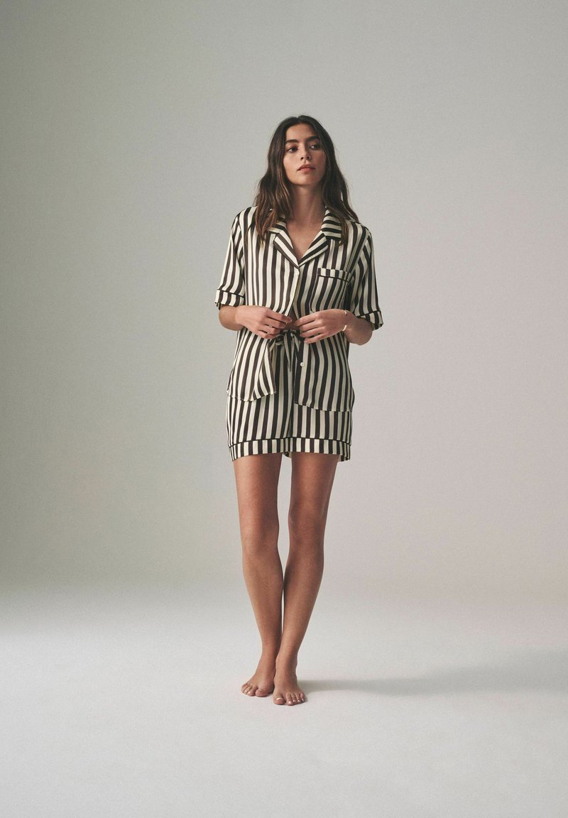Zwart-wit gestreepte korte pyjama set met een kraag, korte mouwen, een zak en een tailleband. Zachte stof met een gladde textuur.