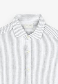 Chemise à rayures verticales blanches et gris clair avec col, boutonnée, vue de la poitrine vers le haut, étiquette de la marque « Scalpers » visible à l'intérieur du col.