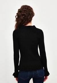 Czarny prążkowany sweter z długimi rękawami, dopasowany fason i falbaniasty dół. Miękka faktura i minimalistyczne detale. Widok od tyłu.
