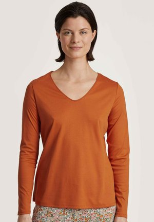 Langdraagbare, v-hals shirt van effen oranje stof met een soepele textuur en een aansluitende silhoeët. Gecombineerd met een rok met bloemenpatroon.