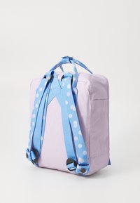 Mochila de tecido roxa com alças em padrão de bolinhas azuis, forma retangular e pega na parte superior. Possui ferragens em plástico e textura suave.