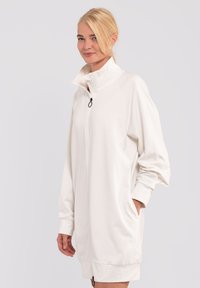Abito felpa bianco con zip, collo alto, maniche lunghe, tasche laterali e polsini a costina. Tessuto morbido con una silhouette rilassata.