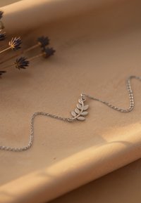 Collana con pendente a forma di foglia in argento, caratterizzata da una delicata catena. Il pendente presenta un design a foglia con dettagli lisci e lucidi su uno sfondo morbido.