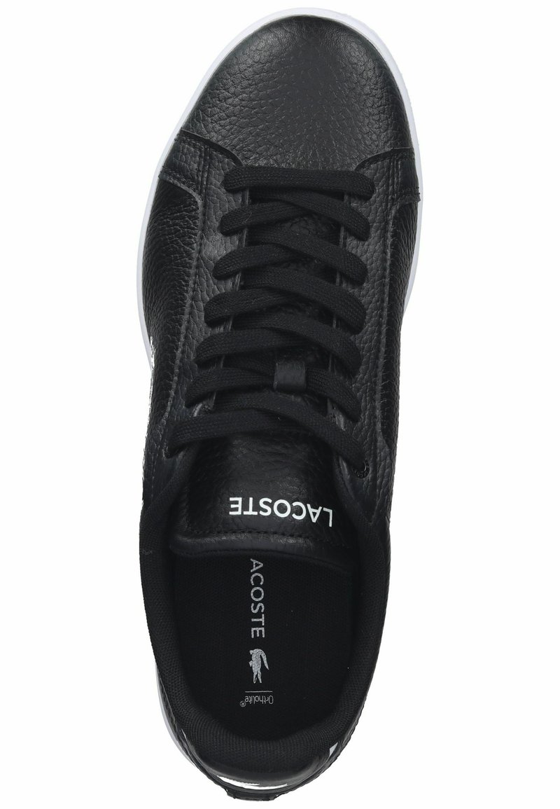 Sneaker en cuir noir avec tige texturée, bout arrondi et semelle en caoutchouc blanc. Dispose de lacets noirs et de la marque "Lacoste" sur la languette.