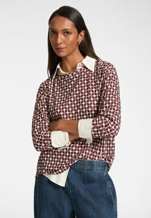 Maglietta a maniche lunghe con un design a motivo color bordeaux. Collo e polsini bianchi. Vestibilità rilassata con una leggera caduta. Indossata con pantaloni di jeans.