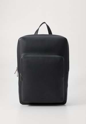 Musta nahkainen reppu, jossa on suorakulmainen muoto, etupuolella vetoketjullinen tasku ja yläranka. Tasainen pinta, jossa on hienovaraiset ompeleet.